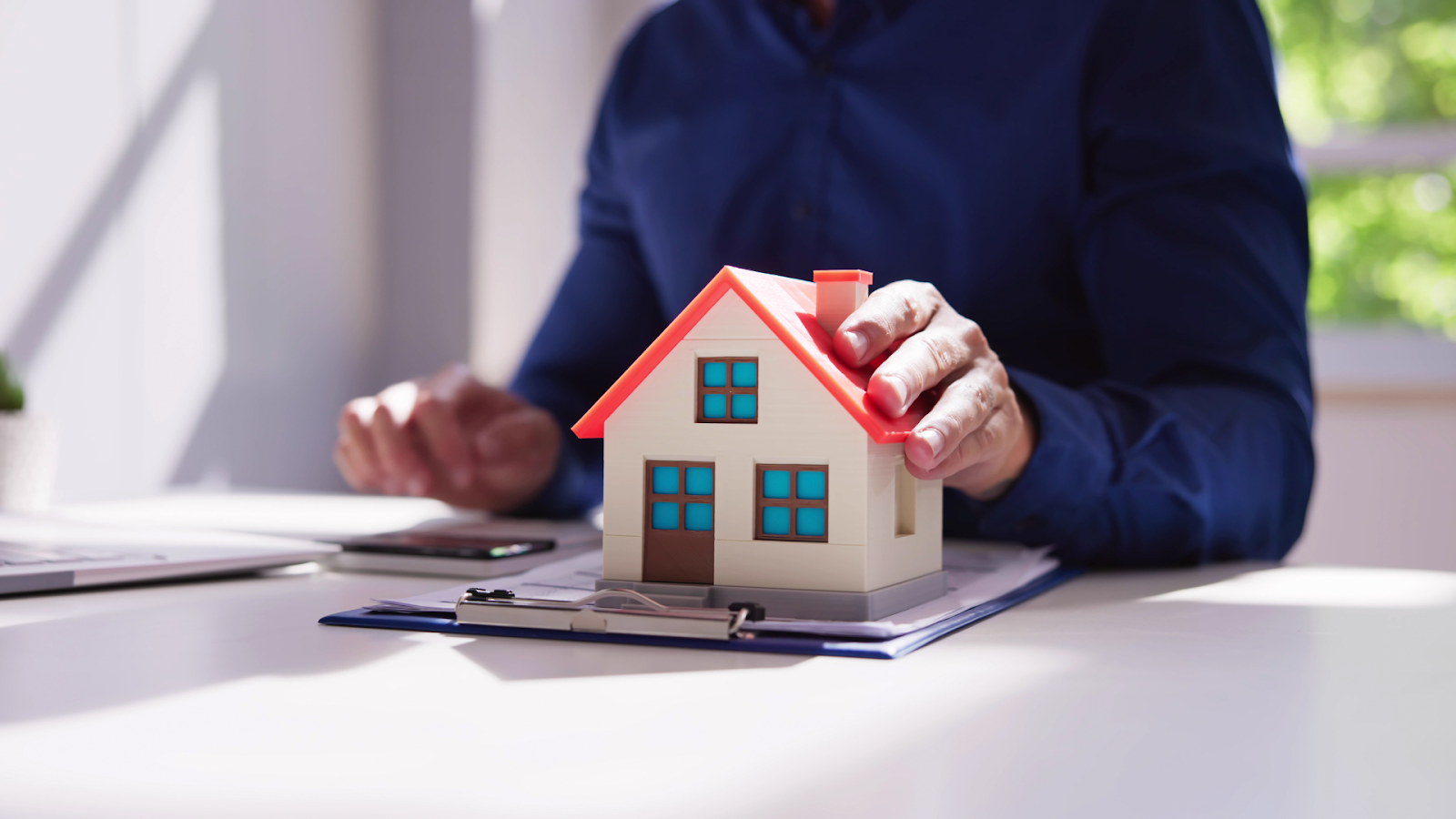 Tax agent holding miniature home with property documents underneath