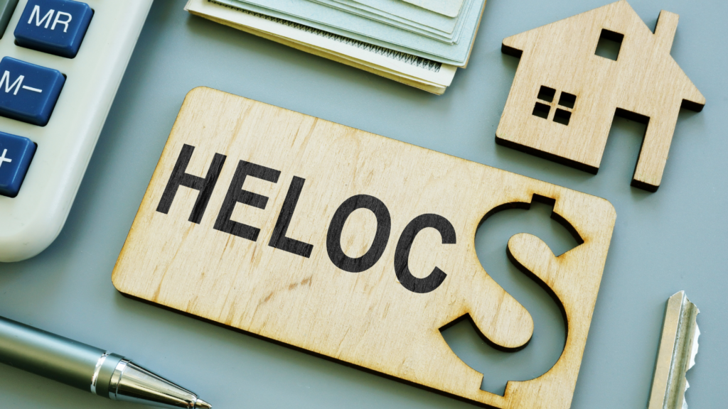 Wooden sign with the word HELOC next to a small house figurine and calculator representing a Home Equity Line of Credit